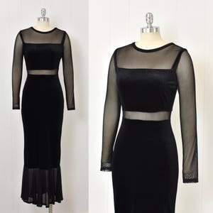 May include: Black velvet maxi dress with sheer mesh long sleeves and neckline. The dress features a sheer midriff panel and a flared chiffon hem. The dress is displayed on a mannequin.