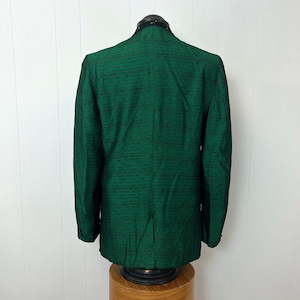 Może przedstawiać: Zielony blazer w ciemnym odcieniu z czarno-zielonym paskowanym wzorem. Blazer ma wycięty kołnierz i długie rękawy.