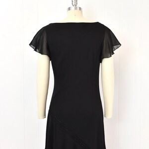 May include: A black dress with a square neckline and short, sheer flutter sleeves. The dress has a fitted bodice and a flared skirt. A diagonal line of small beads accents the front of the skirt. The dress is displayed on a mannequin.