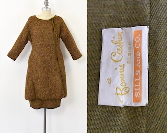 May include: A brown and pink tweed dress with a long sleeve and a tie at the neck. The dress has a label that reads "a Bonnie Cashin Design Sills and Co."