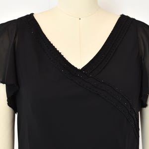 May include: Black V-neck top with flutter sleeves. The neckline and upper bodice feature a beaded trim. The sleeves are made of a sheer, flowing fabric. The top is displayed on a mannequin.