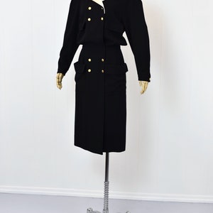 May include: A black dress with a white collar and gold buttons. The dress has a double-breasted closure and large pockets on the sides.