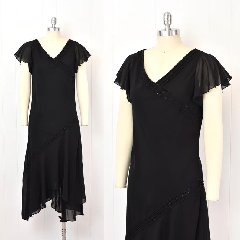 May include: Black vintage dress with a V-neck and flutter sleeves. The dress has a diagonal beaded detail and an asymmetrical hem. The dress is displayed on a mannequin.