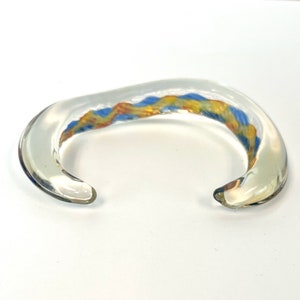 May include: A clear glass bangle bracelet with a colorful swirl of blue, yellow, and orange glass.