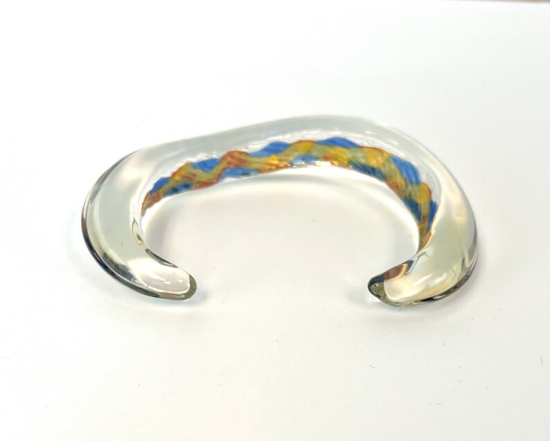 May include: A clear glass bangle bracelet with a colorful swirl of blue, yellow, and orange glass.
