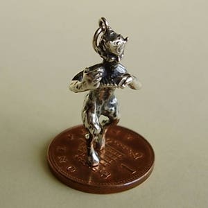 Puede incluir: Un amuleto de plata de un sátiro tocando un instrumento musical, de pie sobre una moneda de color cobre con la inscripción "ONE POUND".