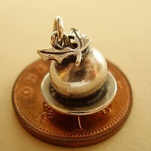 May include: Silver charm of a Christmas pudding with a holly sprig on top, sitting on a penny.