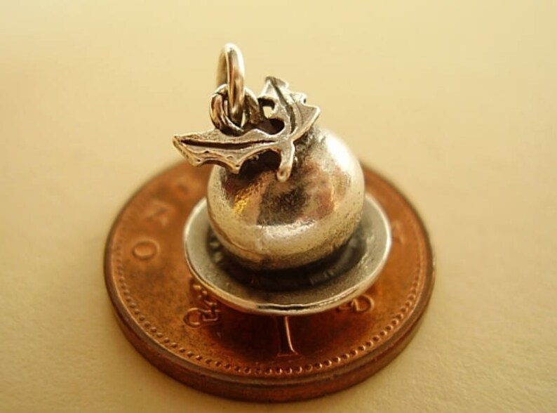 May include: Silver charm of a Christmas pudding with a holly sprig on top, sitting on a penny.
