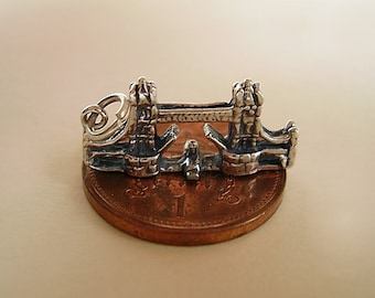 May include: Silver charm of the Tower Bridge in London, England. The charm is about the size of a US penny.