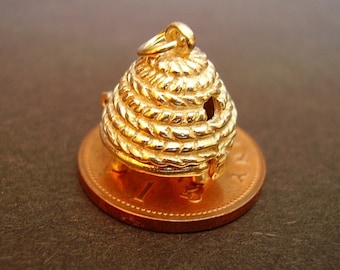May include: A gold-coloured beehive charm with a detailed design. The charm is sitting on a copper-coloured coin.