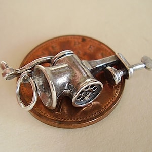 May include: Silver charm in the shape of a vintage meat grinder. The charm is sitting on a penny for size comparison.