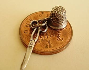 Puede incluir: Encanto de plata con un dedal y un par de tijeras, descansando sobre una moneda británica de una libra.
