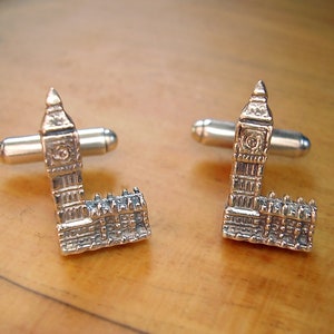 May include: A pair of silver cufflinks featuring a miniature replica of the Houses of Parliament, also known as Big Ben, in London, England.