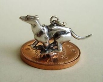 Puede incluir: Encanto de plata de un galgo corriendo, mostrado en un centavo para comparar el tamaño.