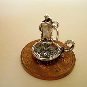 Puede incluir: Encanto de plata de un candelabro con una vela en un plato peque&ntilde;o. El encanto est&aacute; sentado en una moneda de un penique brit&aacute;nico.