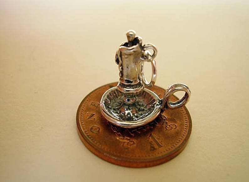 Puede incluir: Encanto de plata de un candelabro con una vela en un plato peque&ntilde;o. El encanto est&aacute; sentado en una moneda de un penique brit&aacute;nico.
