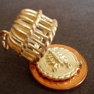 May include: Gold charm of a scorpion in a cage, with a copper coin underneath. The cage is open and the scorpion is visible.