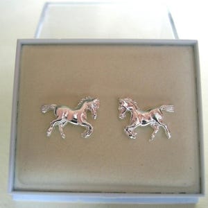 May include: A pair of silver horse earrings in a white box. The horses are facing forward with their heads held high.