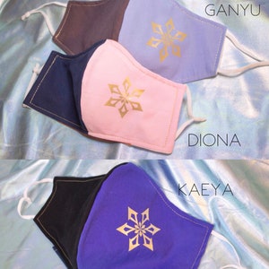 Pode incluir: Tr&ecirc;s m&aacute;scaras faciais reutiliz&aacute;veis com diferentes combina&ccedil;&otilde;es de cores e um design de floco de neve dourado. As m&aacute;scaras s&atilde;o etiquetadas como "Ganyu", "Diona" e "Kaeya".