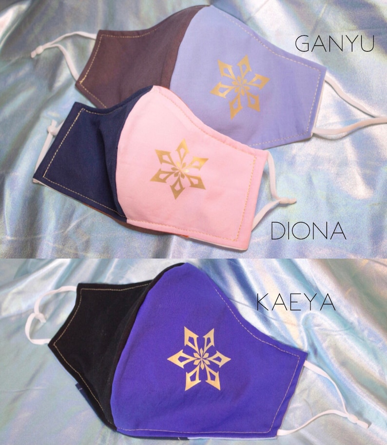 Pode incluir: Tr&ecirc;s m&aacute;scaras faciais reutiliz&aacute;veis com diferentes combina&ccedil;&otilde;es de cores e um design de floco de neve dourado. As m&aacute;scaras s&atilde;o etiquetadas como "Ganyu", "Diona" e "Kaeya".