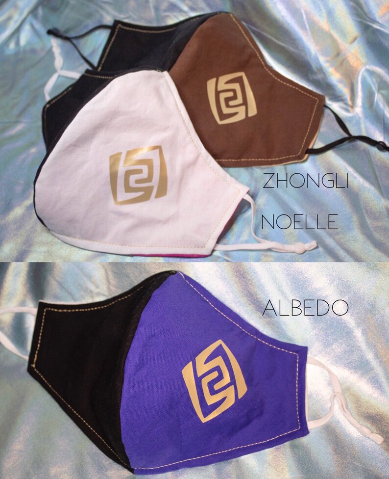 Pode incluir: Tr&ecirc;s m&aacute;scaras faciais de tecido preto, branco, marrom e roxo. Cada m&aacute;scara tem um design geom&eacute;trico dourado e os nomes "Zhongli", "Noelle" e "Albedo" escritos nelas.