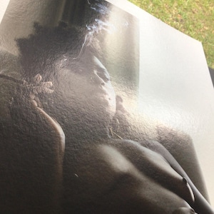 May include: A monochrome photograph of a person's upper body. The image has a soft focus, with gentle shading and details. Wisps of smoke are visible near the head, adding a sense of atmosphere.