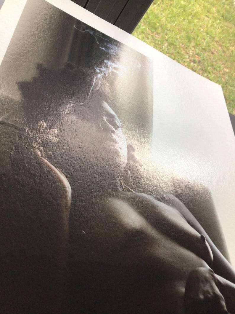 May include: A monochrome photograph of a person's upper body. The image has a soft focus, with gentle shading and details. Wisps of smoke are visible near the head, adding a sense of atmosphere.