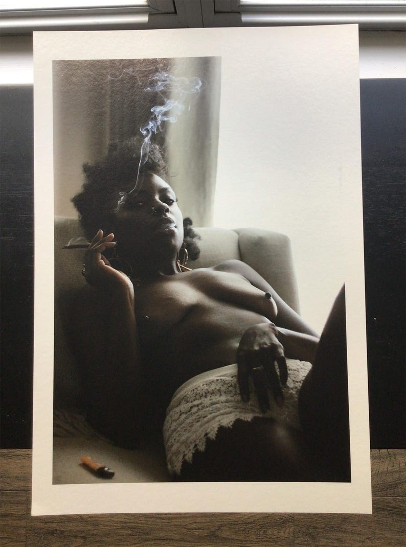 May include: A black and white photograph of a person reclining on a chair, smoking. The person is wearing a white lace garment. Smoke rises from the cigarette. A lighter is on the surface.