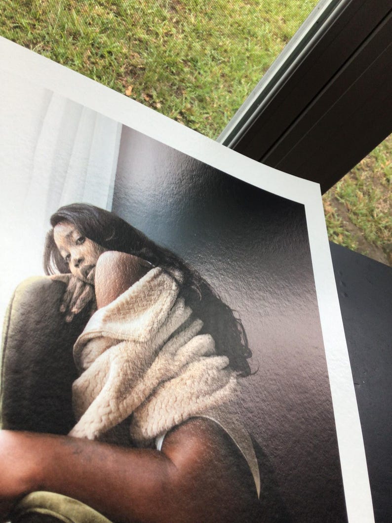 May include: A print of a person with long dark hair, wrapped in a beige blanket, sitting in a green chair. The print has a glossy finish and is set against a dark background.