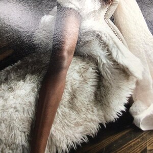May include: A plush, off-white faux fur throw blanket with a thick, shaggy texture. The blanket features a soft, dense pile and a light cream colour throughout, providing a voluminous and cosy appearance with its long, synthetic fibres.