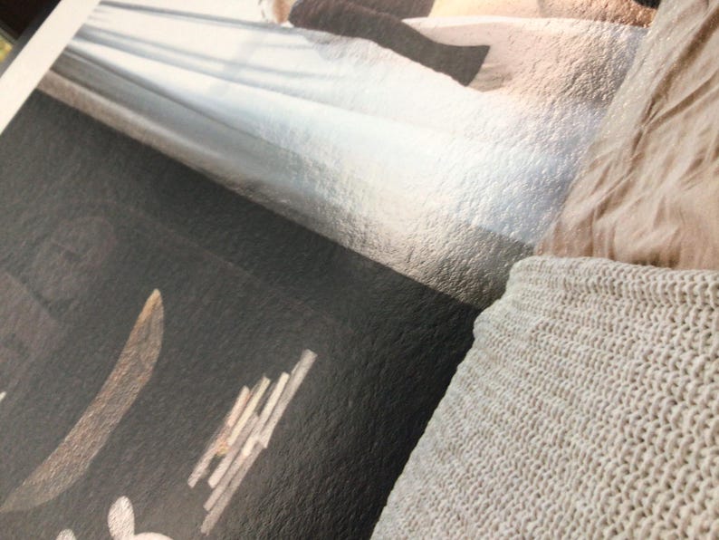 May include: Close-up of a textured, dark surface with a light-colored design and text. A light-colored knitted blanket is in the lower right corner. The image has a soft, muted color palette.