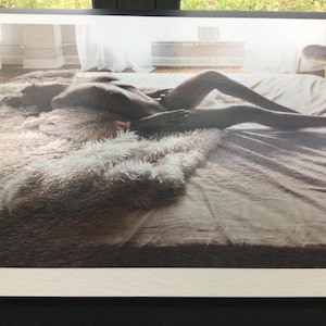 Pode incluir: Fotografia a preto e branco de uma pessoa deitada numa cama. A cama &eacute; coberta com um tapete fofo de cor clara e um len&ccedil;ol liso de tom neutro. A pessoa est&aacute; posicionada horizontalmente, com as pernas estendidas.