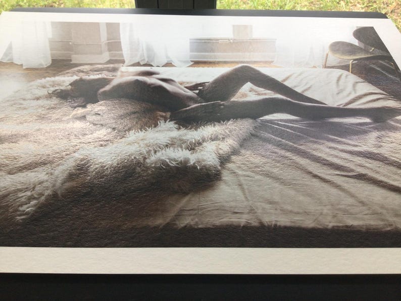 Pode incluir: Fotografia a preto e branco de uma pessoa deitada numa cama. A cama &eacute; coberta com um tapete fofo de cor clara e um len&ccedil;ol liso de tom neutro. A pessoa est&aacute; posicionada horizontalmente, com as pernas estendidas.