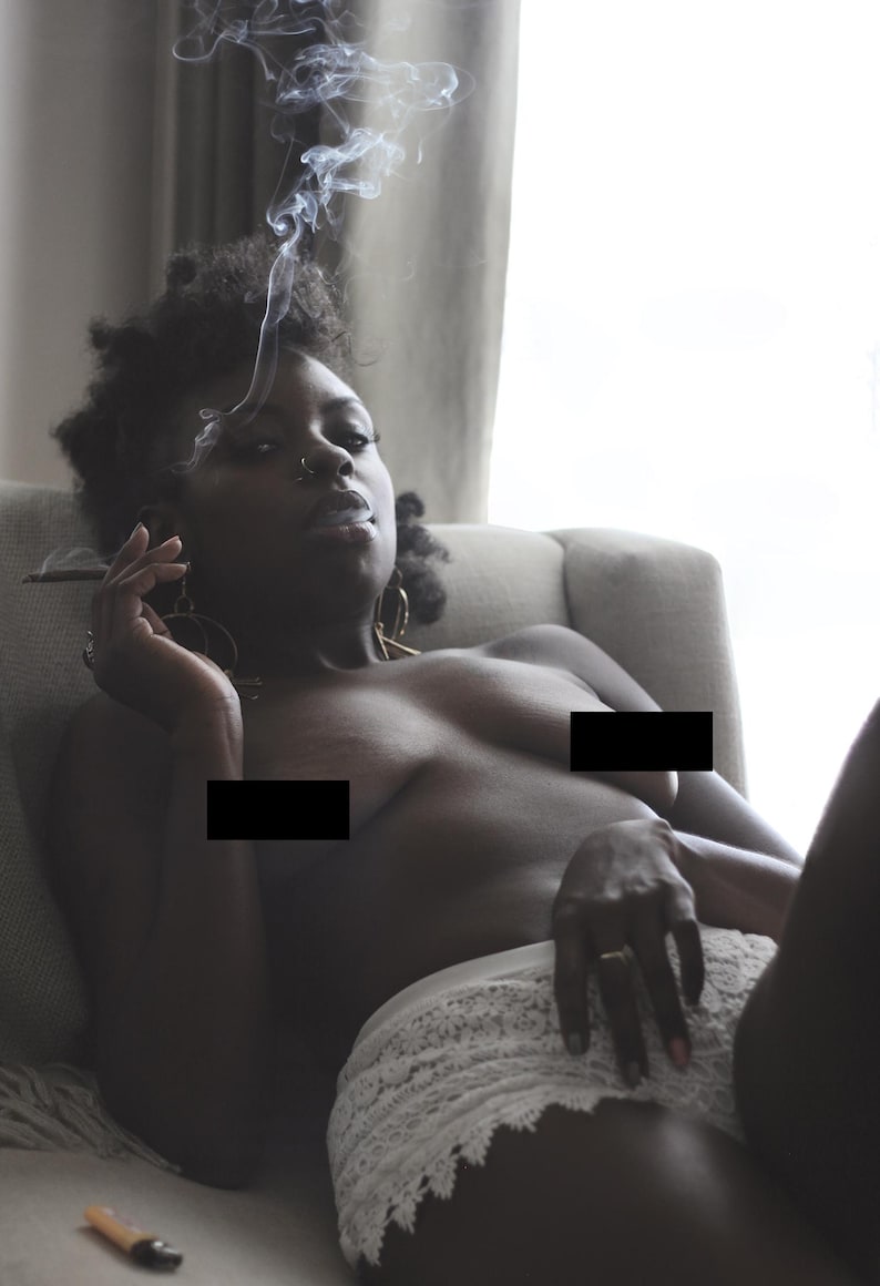 May include: A person reclines on a light-coloured armchair, exhaling smoke. They wear a white lace garment. The image is softly lit, with smoke rising against a window. Accessories include gold earrings and a nose ring.