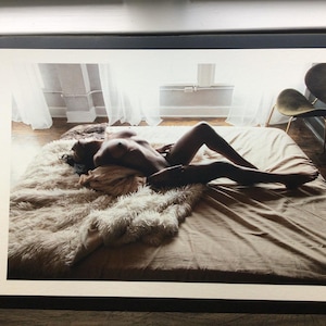 Pode incluir: Fotografia de uma pessoa deitada numa cama. A cama &eacute; coberta com um len&ccedil;ol bege e um tapete fofo, creme. A pessoa est&aacute; nua, com as pernas estendidas. A sala tem luz natural.
