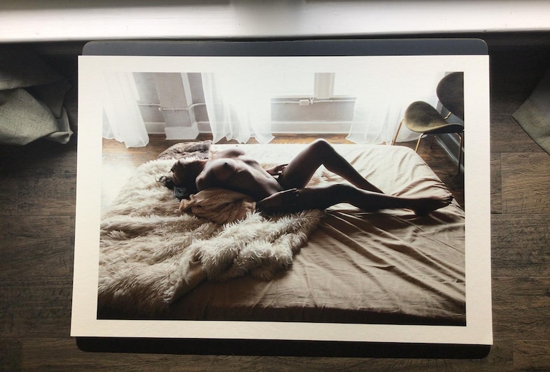 Pode incluir: Fotografia de uma pessoa deitada numa cama. A cama &eacute; coberta com um len&ccedil;ol bege e um tapete fofo, creme. A pessoa est&aacute; nua, com as pernas estendidas. A sala tem luz natural.