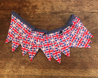 May include: A bunting with red, white, and blue Union Jack flags. The flags are sewn together with a navy blue and white polka dot ribbon.