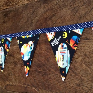 Peut inclure: Une bannière en tissu bleu et noir avec une bordure blanche à pois. La bannière présente un motif répété d'un robot et les mots "Star Wars".