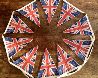 May include: A bunting with nine triangular flags featuring the Union Jack design. The flags are sewn together with white fabric and are strung together in a circle.