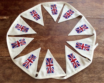 May include: A string of cream-colored triangular flags, each displaying the Union Jack in red, white, and blue. The bunting is arranged in a circular pattern, perfect for patriotic celebrations or themed events.
