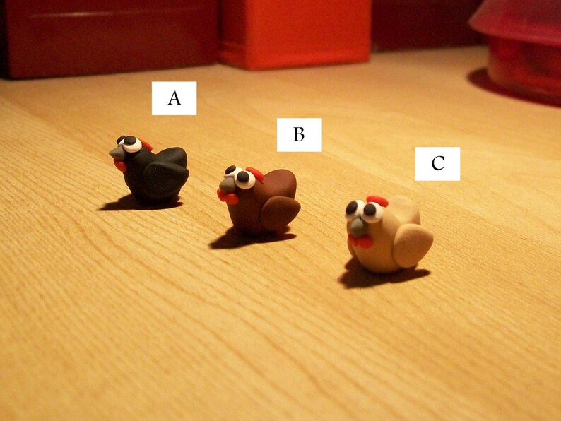 May include: Three small clay figurines of chickens. The first chicken is black, the second is brown, and the third is beige. The chickens are labeled A, B, and C.