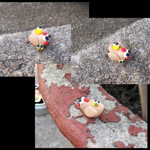 May include: Three small, brown clay figurines of turkeys with yellow, red, and black details. The turkeys are sitting on a gray, textured surface.
