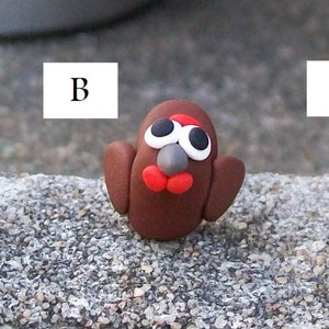 May include: Three small clay figurines of birds, each with a different color: black, brown, and beige. The birds have white eyes, red beaks, and gray noses.
