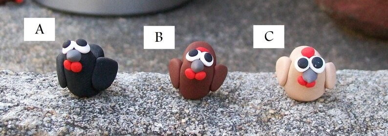 May include: Three small clay figurines of birds, each with a different color: black, brown, and beige. The birds have white eyes, red beaks, and gray noses.