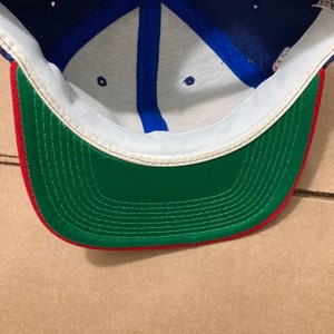 Op de afbeelding: De binnenkant van een blauwe, witte en rode baseballpet. De pet heeft een groen zweetband met rode stiksels.