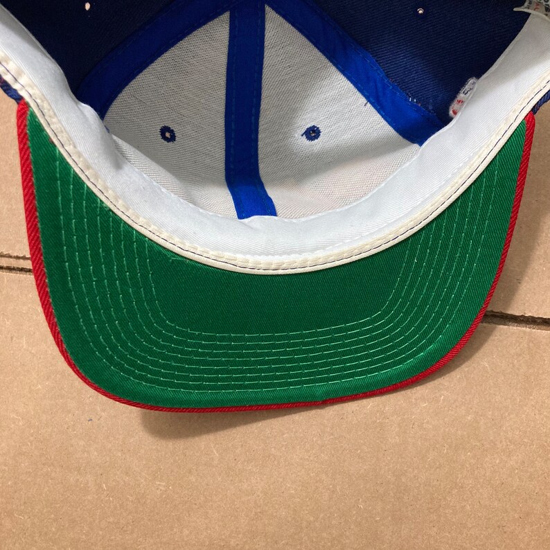 Op de afbeelding: De binnenkant van een blauwe, witte en rode baseballpet. De pet heeft een groen zweetband met rode stiksels.