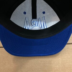 Puede incluir: Gorra de b&eacute;isbol azul y negra con interior blanco. El interior tiene un logotipo bordado blanco con el texto "NBA".