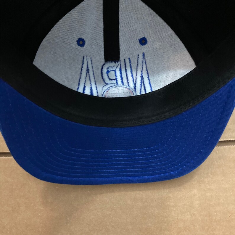 Puede incluir: Gorra de b&eacute;isbol azul y negra con interior blanco. El interior tiene un logotipo bordado blanco con el texto "NBA".