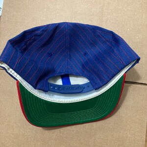 Op de afbeelding: Blauwe en rode gestreepte baseballpet met een groene en rode onderkant. De pet heeft een blauwe verstelbare band.
