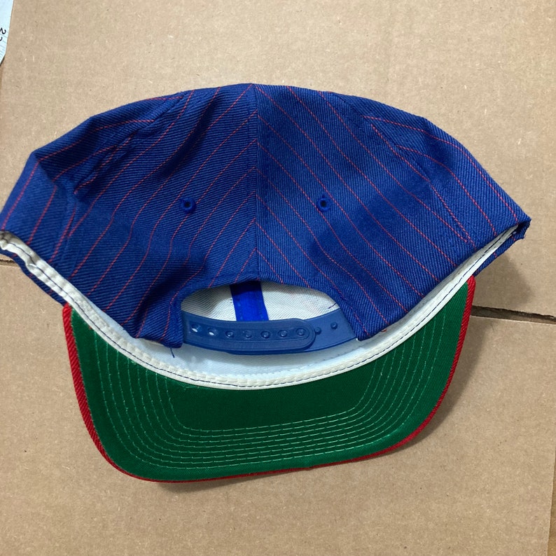 Op de afbeelding: Blauwe en rode gestreepte baseballpet met een groene en rode onderkant. De pet heeft een blauwe verstelbare band.